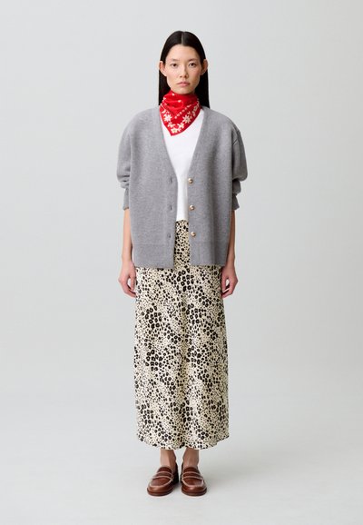 Cárdigan gris de punto con botones dorados, camiseta blanca, falda larga con estampado de leopardo y mocasines marrones. Bufanda roja con patrón blanco.