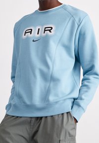 Ljusblå sweatshirt med rund hals, utrustad med en framträdande "AIR" grafik i svart och grått. Tillverkad av mjukt material med ribbade ärmslut.