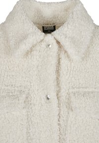 Veste sherpa blanche texturée avec col, boutons-pression et deux poches avant, taille XS, étiquette visible à l'intérieur du col.