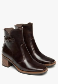 Donkerbruine leren enkelboots met een gladde afwerking, zij-elastische panelen en een decoratieve band met een metalen gesp rond de enkel. Blokhak ontwerp.