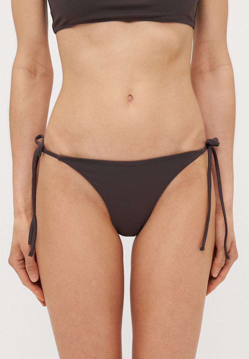 Brune bikinibukse med knyttekanter, laget av glatt og elastisk materiale. Har en smal skjæring og design med minimal dekning.