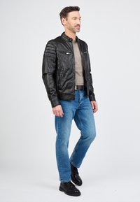 Schwarze Lederjacke mit gesteppten Schultern, silbernen Reißverschlusstaschen, kombiniert mit einem hellen Pullover und blauen Jeans. Getragen mit schwarzen Schnürstiefeln.