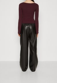 Prążkowany bordowy top z długim rękawem w połączeniu z wysokim stanem czarnych szerokich spodni z ekoskóry. Gładka faktura i luźny krój.