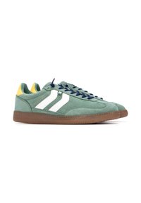 Zapatillas de suede verde con franjas blancas, cordones azul marino y detalles amarillos en el talón. Suela de goma marrón con agarre texturizado.
