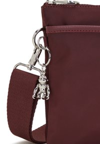 Borsa a tracolla bordeaux realizzata in nylon resistente con una clip argentata e un ciondolo a forma di robot metallico attaccato. Presenta una tracolla testurizzata.