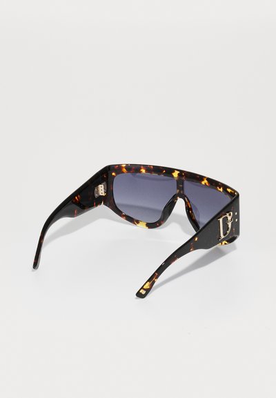 Lunettes de soleil larges et sombres en écaille de tortue avec des verres dégradés, présentant un design géométrique audacieux et un petit accent en or sur la branche.