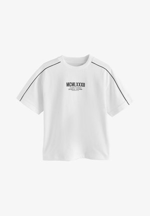 Witte katoenen T-shirt met korte mouwen, met een zwarte afbeelding van "MCMLXXXII" en extra tekst op de borst, omlijnd met zwarte bies.