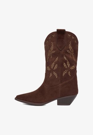 Hnědá semišová kovbojská bota s nízkým naskládaným podpatkem a dekorativními zlatými cvočky ve tvaru květinových a plamenových vzorů na holení.