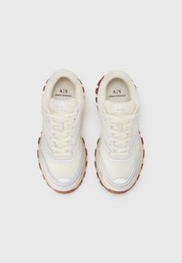 Sneaker color crema con tomaia in mesh e materiale sintetico. Suola in gomma spessa e testurizzata di colore marrone, con un accento argento sui lati.