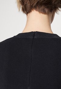 Top nero a coste con scollatura rotonda e una chiusura a zip discreta sul retro, che mettono in risalto una texture liscia e una silhouette aderente.