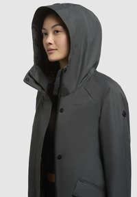 Veste imperméable gris foncé avec capuche, fermeture éclair à l'avant, boutons-pression et doublure à imprimé animal. Conçue en tissu lisse et durable.