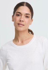 Vit stickad tröja med rund halsringning och långa ärmar, som visar en mjuk textur och en figursydd design.
