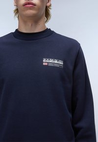 Navyblauwe sweatshirt met een ronde hals, ribgebreide kraag en een groot grafisch logo-opdruk op de linkerkant van de borst. Zachte stofstructuur.