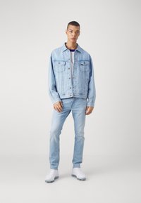 Chaqueta de denim azul claro, corte relajado, con dos bolsillos en el pecho, combinada con jeans azul claro y zapatillas blancas. Textura suave, diseño sencillo.