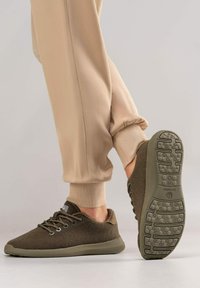 Baskets en cuir brun texturé avec une semelle plate dotée de motifs de traction, associées à un pantalon de jogging beige. Conception à lacets avec des accents de marque subtils.