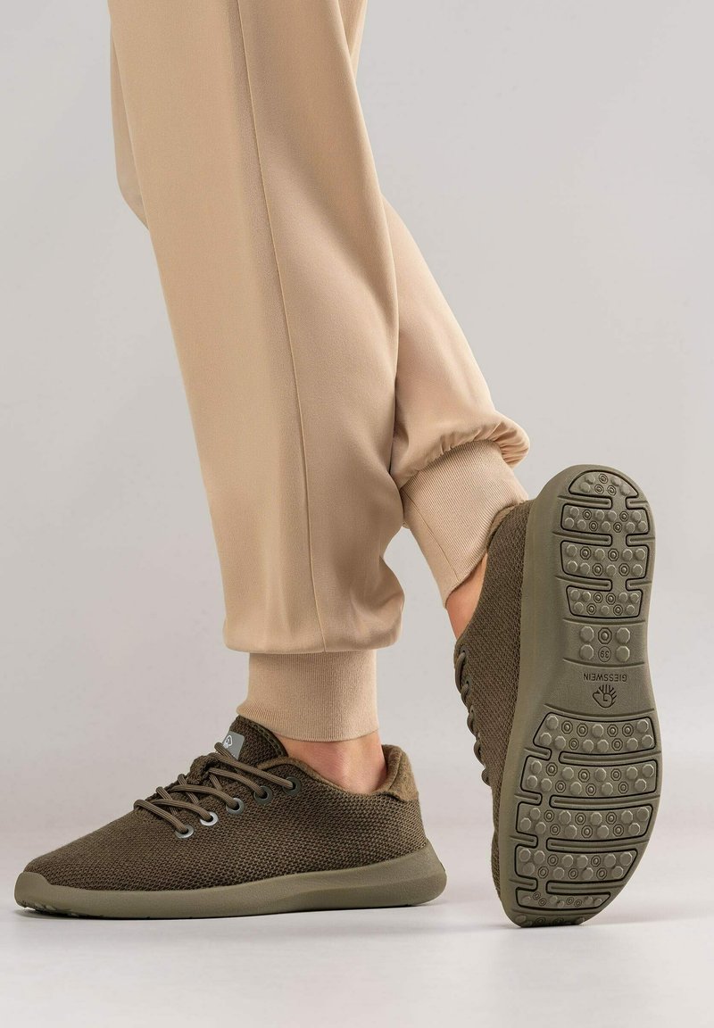 Baskets en cuir brun texturé avec une semelle plate dotée de motifs de traction, associées à un pantalon de jogging beige. Conception à lacets avec des accents de marque subtils.