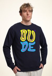 Sudadera de cuello redondo en color marino hecha de algodón, con una vibrante inscripción gráfica "DUDE" en colores amarillo, rosa y azul en la parte delantera.