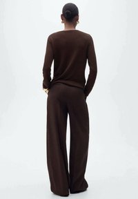 Pull en maille marron à manches longues associé à un pantalon à jambes larges, présentant une texture douce et une coupe décontractée, vu de dos.