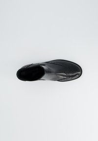 Botín de cuero negro hasta el tobillo con punta redondeada, costuras decorativas y una textura suave. Cuenta con un tacón bajo y sutiles perforaciones.
