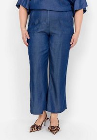 Jeansbyxor med vida ben i mörkblått, med två framfickor och kontrasterande sömmar. Kombineras med klackar med spetsig tå i leopardmönster.