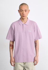 Polo shirt lilas clair en tissu doux, avec un col classique, des manches courtes et un petit logo blanc.