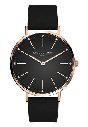 Montre noire avec un cadran rond, accents en or rose, design minimaliste et marqueurs d'heure scintillants. Équipée d'un bracelet texturé noir.