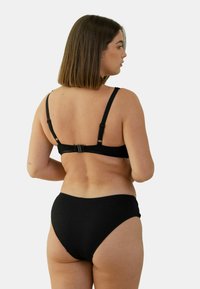 Ensemble de bikini noir en tissu texturé, avec des bretelles ajustables et un détail de fermoir dans le dos. Bas taille haute avec une finition lisse.