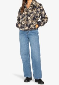 Sudadera de forro polar con estampado floral en azul marino, crema y amarillo. Presenta un cuello con media cremallera y mangas largas. Combinada con vaqueros azul claro.