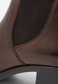 Stivaletto in pelle marrone con pannelli laterali elastici, design elegante, dettagli di cucitura discreti e un tacco nero basso.