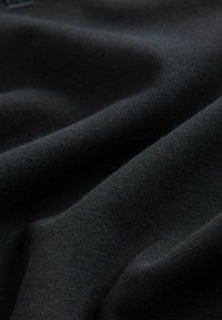 Čierna tkanina s hladkou textúrou, obsahujúca vlnky a záhyby. Materiál sa zdá byť mäkký a elastický, vhodný na oblečenie alebo čalúnenie.
