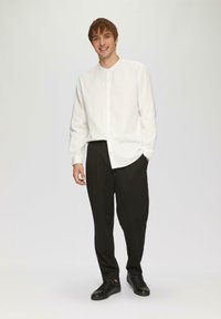 Camisa blanca de manga larga con botones, pantalones negros de corte relajado y zapatillas negras, con una textura suave y un diseño simple.