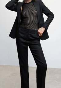 Černý oblek na míru s upnutým, průhledným černým topem s vertikálními pruhy a slim-fit černými kalhotami, minimalistický design na světlém pozadí.
