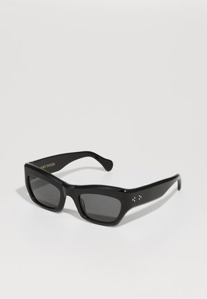 Melni saulesbrilles ar biezu, taisnstūra formu, tumšiem lēcu tonī, un maigi dekoratīvi akcenti uz tempļiem. Matēta apdare.
