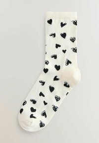 Șosete până la genunchi, crem, cu un model repetitiv de inimioare negre, realizate dintr-un material tricotat moale, cu manșetă nervurată și vârf întărit.