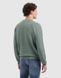 Groen textuurtrui met geribde manchetten en zoom, met een ronde halslijn en een losse pasvorm, gedragen over blauwe jeans.