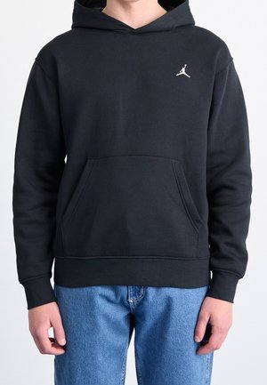Schwarzer Kapuzenpullover mit vorderer Kängurutasche und kleinem weißem Jumpman-Logo auf der linken Brust, getragen mit blauen Jeans.