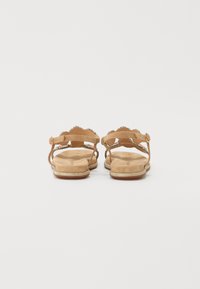 Beige sandaler med rund tå, glatt lærøverdel, dekorativ bølget stropp, og en lett teksturert såle med en subtil glans.