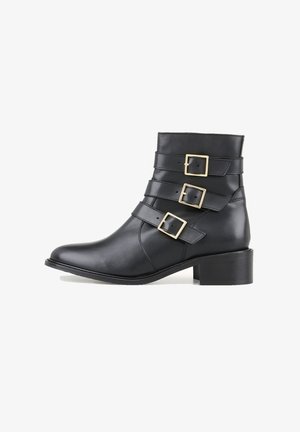 Bottine en cuir noir avec trois brides à boucles dorées, bout arrondi et talon bloc. Texture lisse et design élégant.
