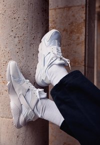 Sneaker bianche con una combinazione di pannelli lisci e testurizzati, che mostrano un design traspirante, chiusura con lacci e accenti perforati.
