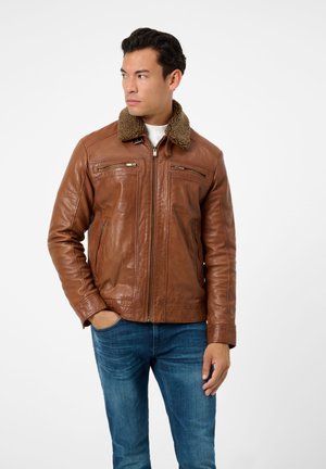 Braune Lederjacke mit einem strukturierten, Kunstfellkragen; verfügt über Reißverschlusstaschen und eine glatte Oberfläche; getragen über einem weißen Hemd und blauen Jeans.