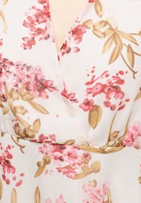 Λευκό ύφασμα με ροζ και καφέ λουλουδένιο μοτίβο που απεικονίζει συστάδες λουλουδιών και φύλλων, με λεπτομέρεια ραφής σε V λαιμόκοψη.