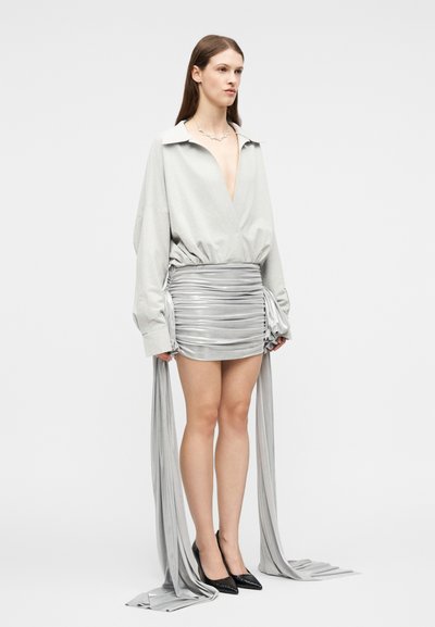 Γυναίκα που φοράει ανοιχτό γκρι μπλούζα με μακριά μανίκια και ρυτιδωτή ασημί μίνι φούστα, συνδυασμένη με μαύρες μυτερές ψηλοτάκουνες γόβες.