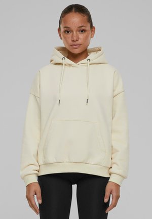 Haut à capuche couleur crème en coton, avec une poche avant, une capuche à cordon et des poignets et un ourlet côtelés. Texture lisse, coupe décontractée.