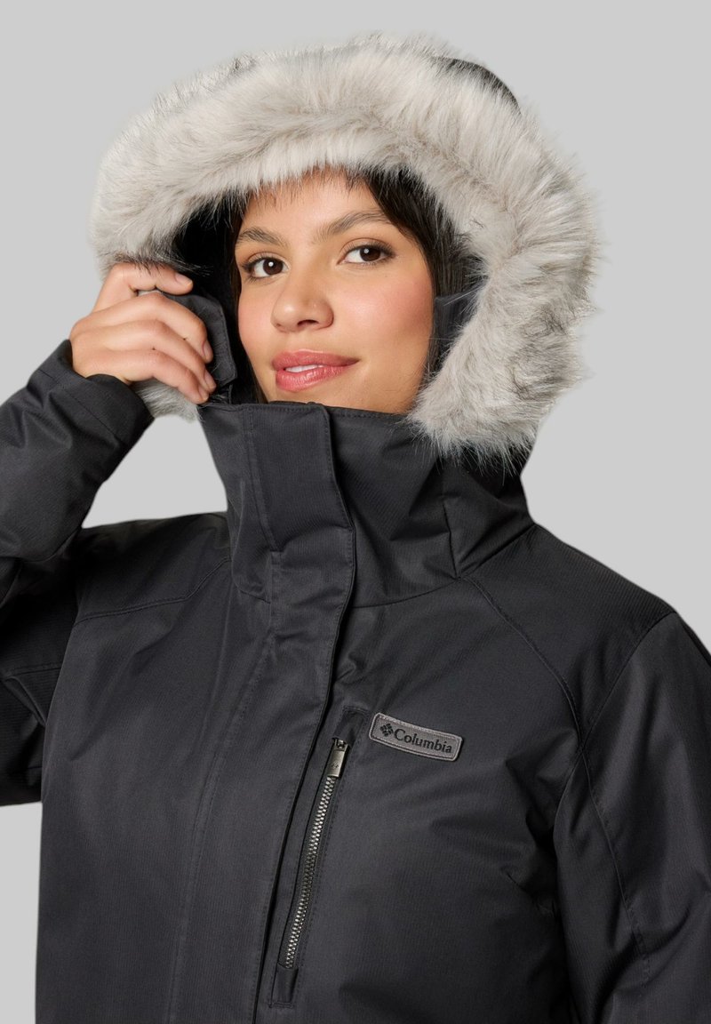 Schwarze isolierte Jacke mit einer mit Kunstfell gefütterten Kapuze, die eine Reißverschlusstasche auf der Brust und ein Logo auf der linken Seite hat. Glatte Textur.