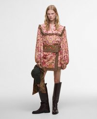 Robe à motifs floraux roses avec un col froncé, des manches longues et une ceinture assortie. Associée à des bottes marron au genou et un chapeau vert.