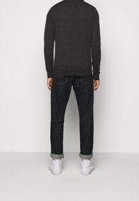 Suéter gris oscuro con cuello redondo, acompañado de vaqueros azul oscuro y zapatillas blancas, visto desde atrás. Los vaqueros tienen los puños remangados.