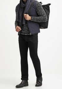 Svarta jeans i kombination med en texturerad gråtröja, marinblå pufferväst och matchande scarf. Inkluderar en svart ryggsäck och ankelstövlar.