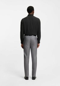 Maglietta nera a maniche lunghe e pantaloni eleganti grigi chiaro con due tasche posteriori, gamba dritta, tessuto liscio e chiusura con bottone, visti da dietro.