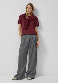 Burgundijas krāsas īsām piedurknēm t-krekls kopā ar pelēkajām svītrainajām platiem biksēm. Modelis valkā šalli ar apkakli, kas pārklāta uz pleciem.