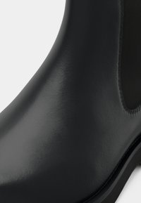 Must hästakinda mustast nahast, millel on sile pind, elastsed külgpaneelid, ümar varvas ja lame kummitald. Suletud detail suurendab tekstuuri.